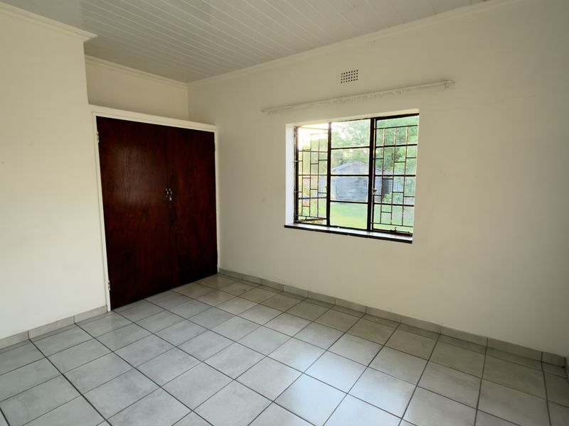 A vacant bedroom featuring tiled flooring, a built-in wooden wardrobe, and a window fitted with security bars.
