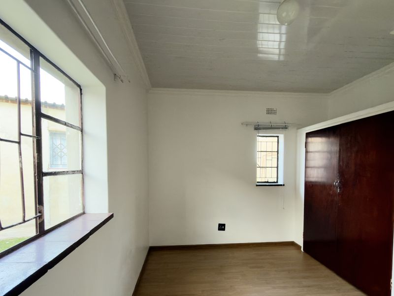 An empty bedroom featuring laminate flooring, built-in cupboards, and steel-framed windows with security bars.