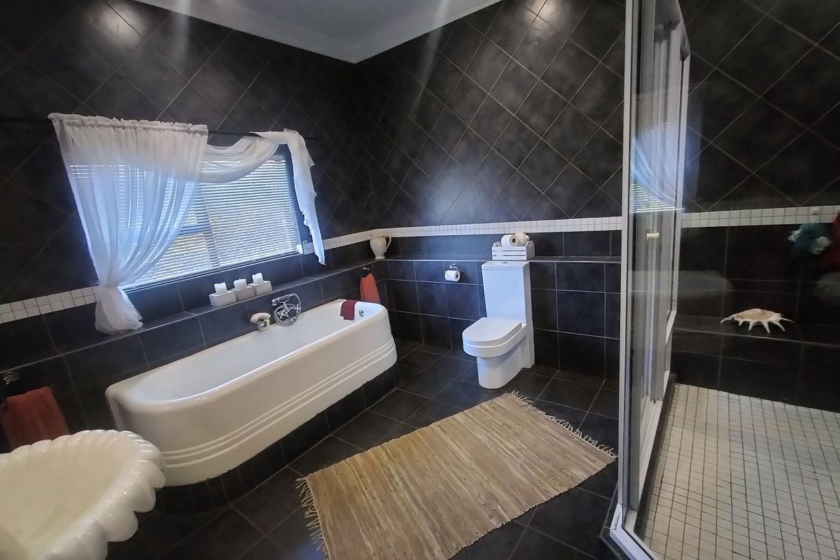 A modern bathroom featuring dark tiled walls, a freestanding bathtub, a separate glass-enclosed shower with a built-in bench, and a toilet.
