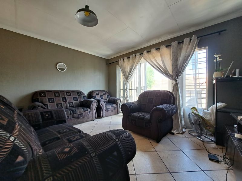 A living room featuring tiled flooring and a sliding glass door with security gate, providing access to the exterior.