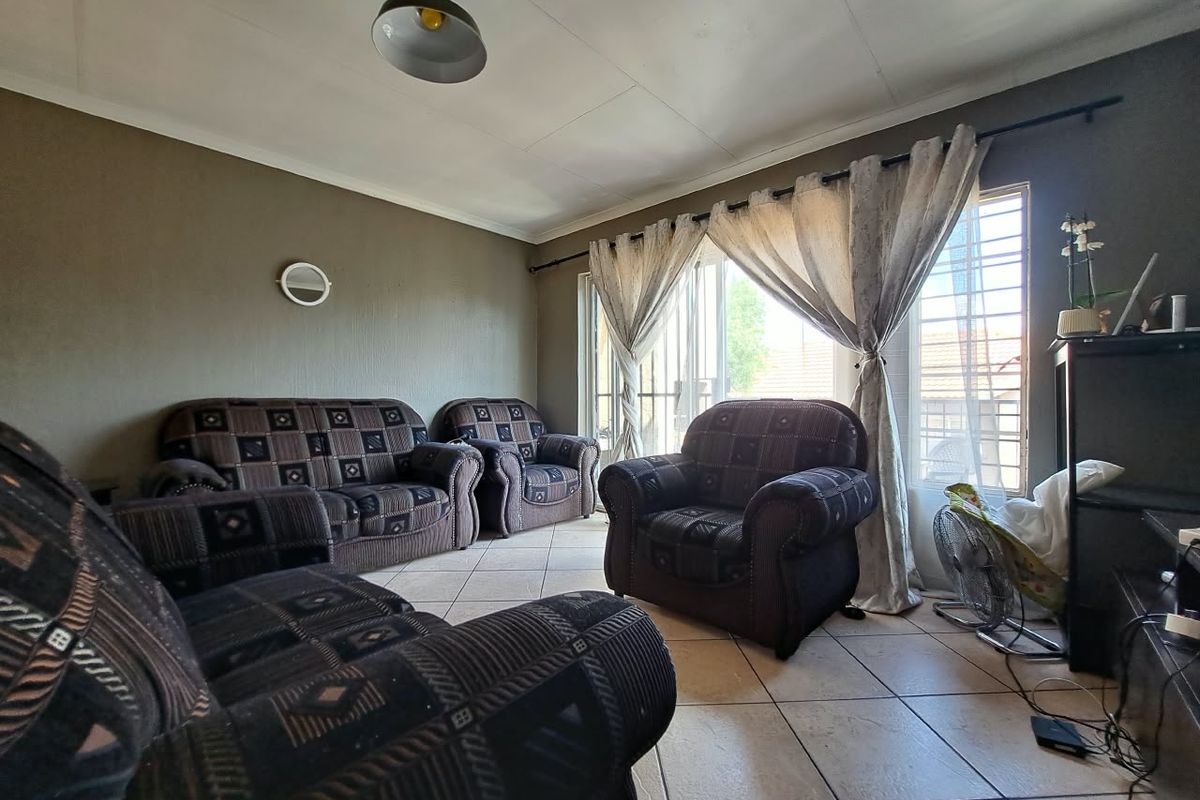 A living room featuring tiled flooring and a sliding glass door with security gate, providing access to the exterior.