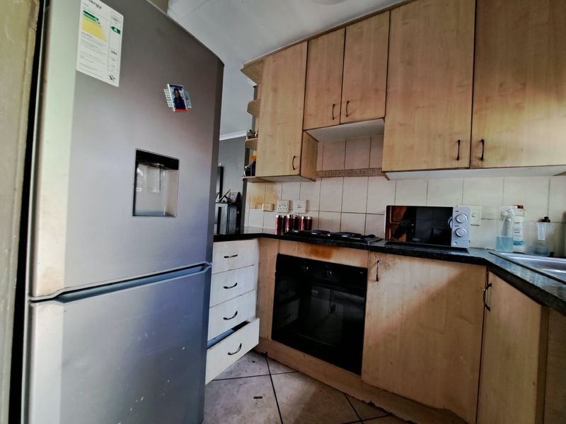 A compact kitchen featuring light wood-tone cabinetry, dark countertops, a built-in oven, and a gas hob, requiring some maintenance and cosmetic updates.