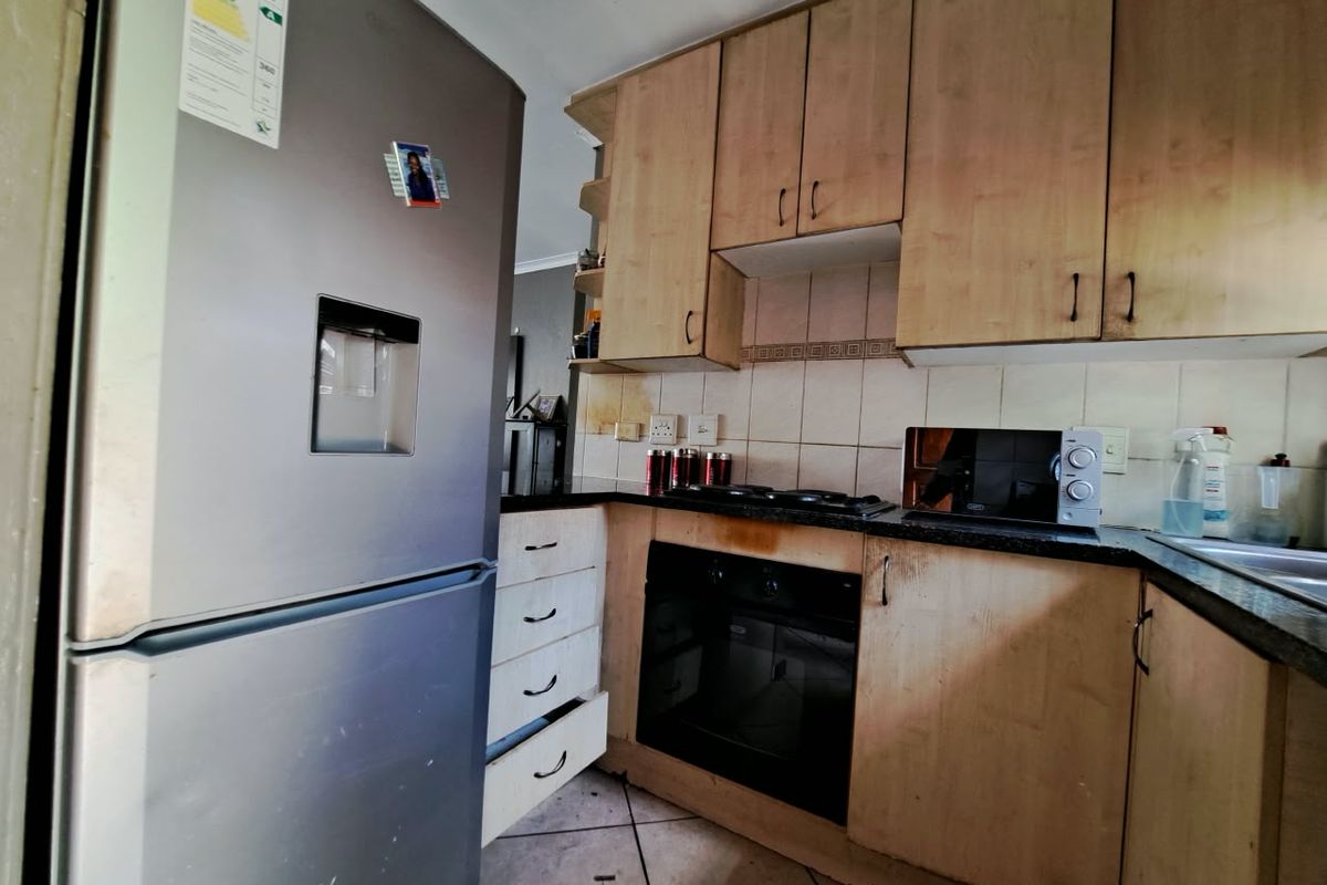 A compact kitchen featuring light wood-tone cabinetry, dark countertops, a built-in oven, and a gas hob, requiring some maintenance and cosmetic updates.