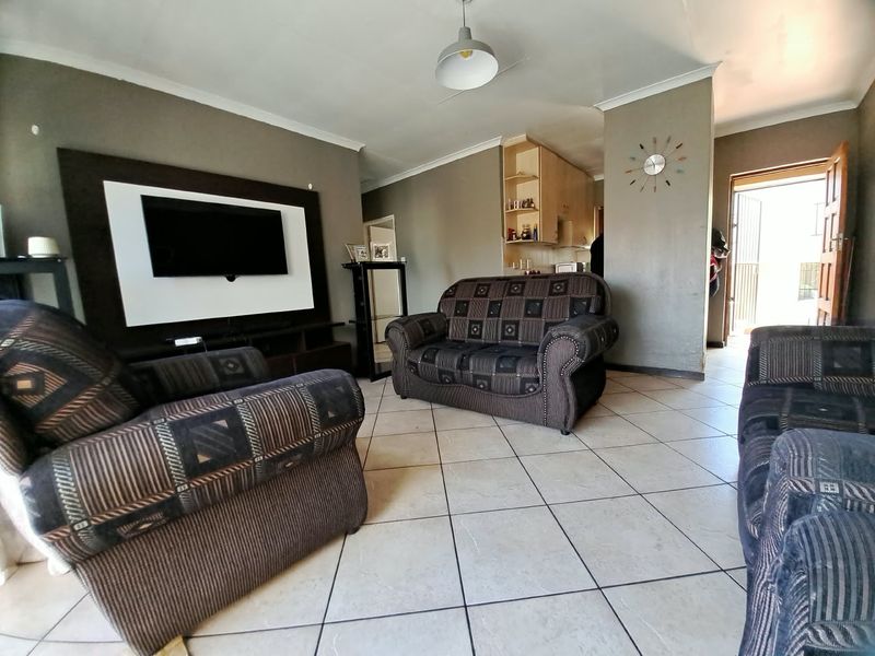 Open-plan living area featuring tiled flooring, a built-in media wall, and direct access to the kitchen and exterior entrance.