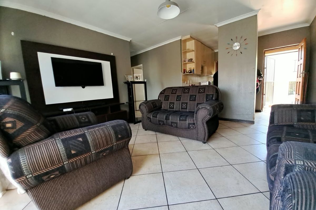 Open-plan living area featuring tiled flooring, a built-in media wall, and direct access to the kitchen and exterior entrance.