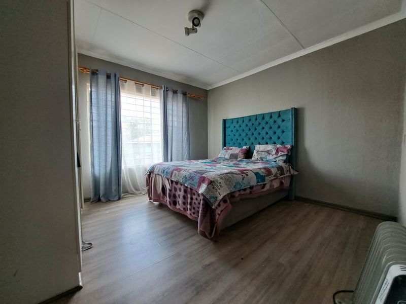 A bedroom featuring laminate flooring, a ceiling-mounted light fixture, and a window with security bars.