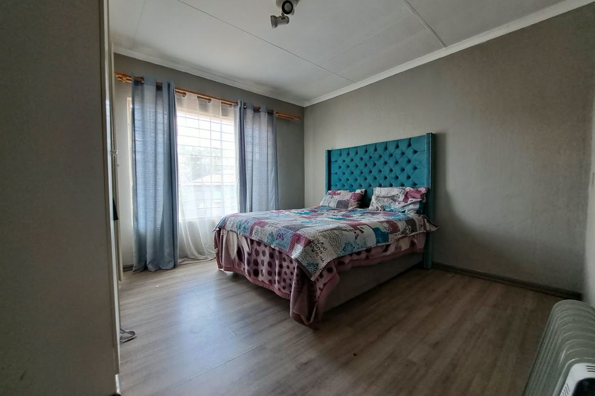 A bedroom featuring laminate flooring, a ceiling-mounted light fixture, and a window with security bars.