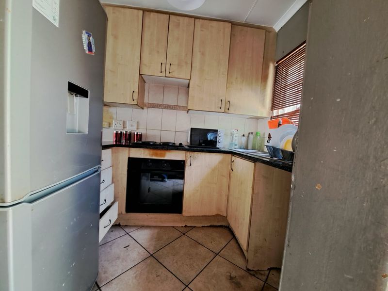 A compact kitchen featuring light wood-tone cabinetry, dark countertops, and tiled flooring. The space requires cosmetic updates to improve its overall condition and appeal.