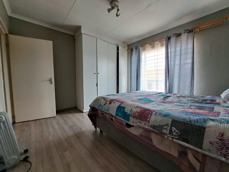 A functional bedroom featuring built-in cupboards, laminate flooring, and security bars on the window, offering a neutral base for personalization.
