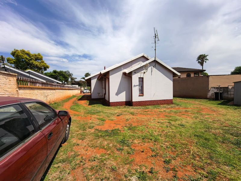 Rear view of the property showing the exterior wall, brick boundary fencing, and surrounding yard space with a television antenna and satellite dish installed.