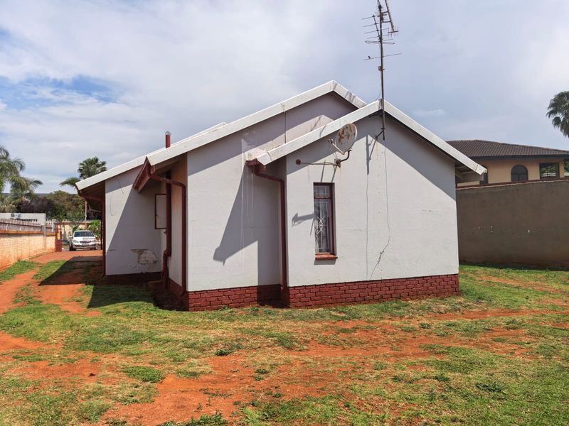 Rear view of the house showing exterior brickwork, guttering, and security bars on the window, set on a large grassed plot.