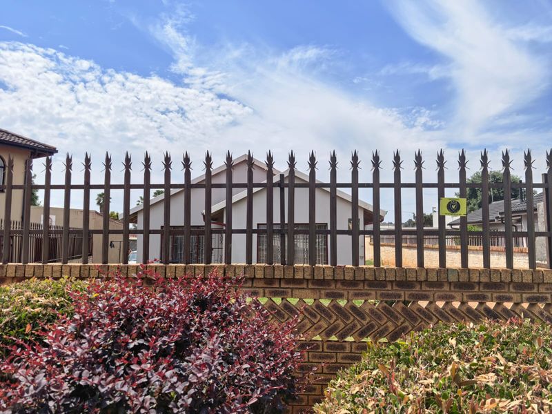 Front view of a residential property featuring a secure brick boundary wall with metal spike fencing and a tiled roof structure.