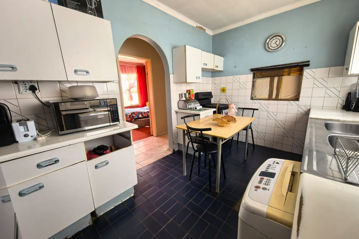 A dated kitchen featuring built-in cabinetry, tiled backsplash, and dark floor tiles, with an arched doorway leading to an adjacent room.