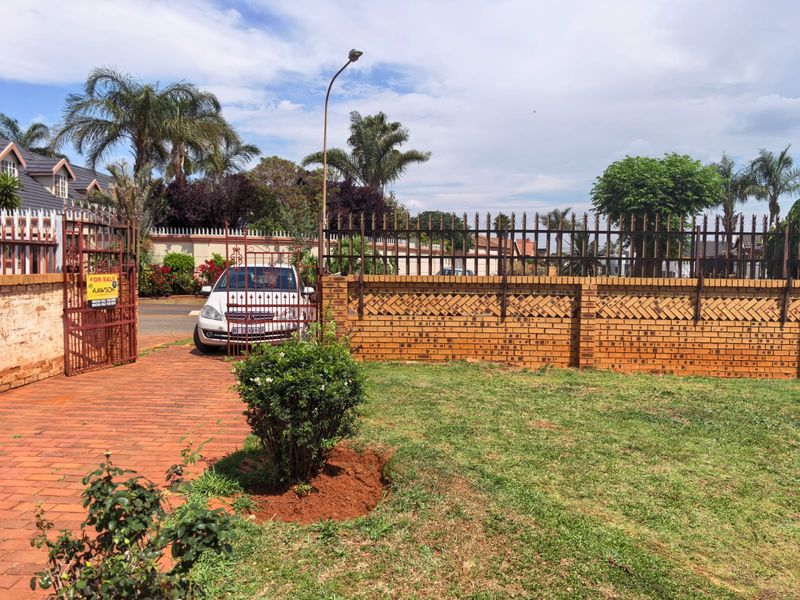 Front exterior view featuring a brick boundary wall with metal security fencing, a paved driveway, and a gated entrance.
