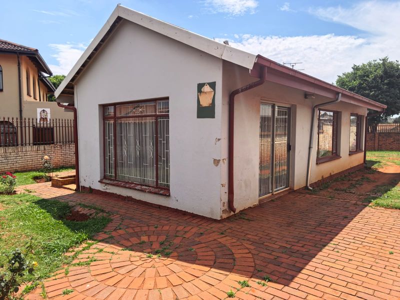 Rear view of the property featuring brick paving, aluminium window frames, and a sliding door entrance, showing signs of exterior wear and maintenance needs.