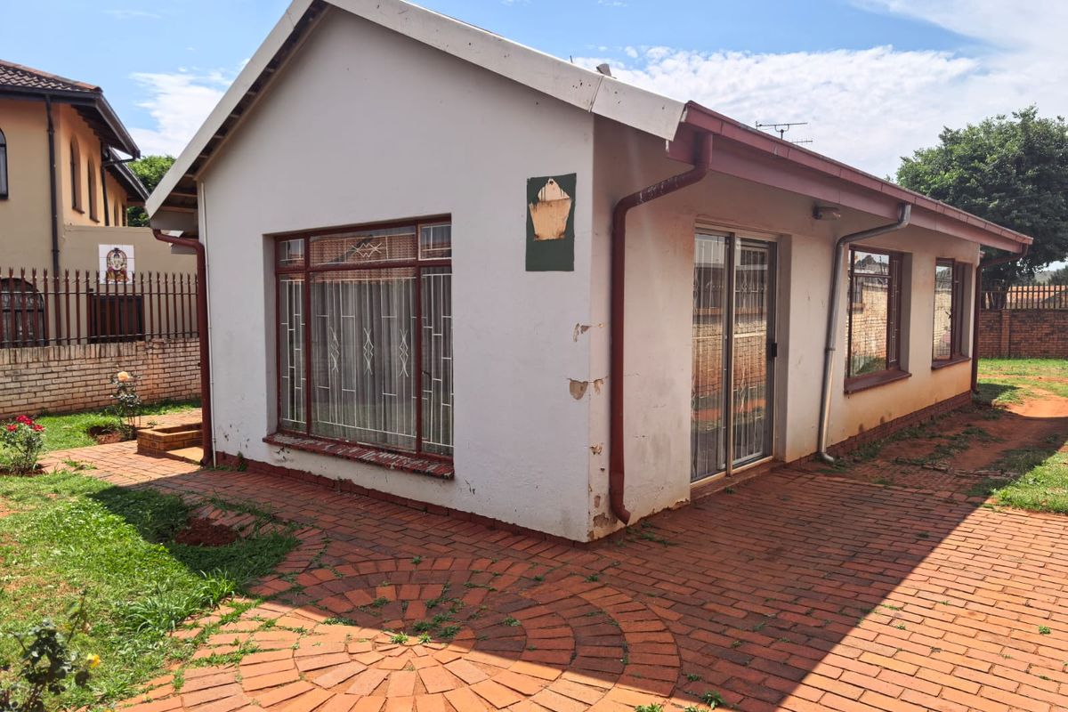 Rear view of the property featuring brick paving, aluminium window frames, and a sliding door entrance, showing signs of exterior wear and maintenance needs.