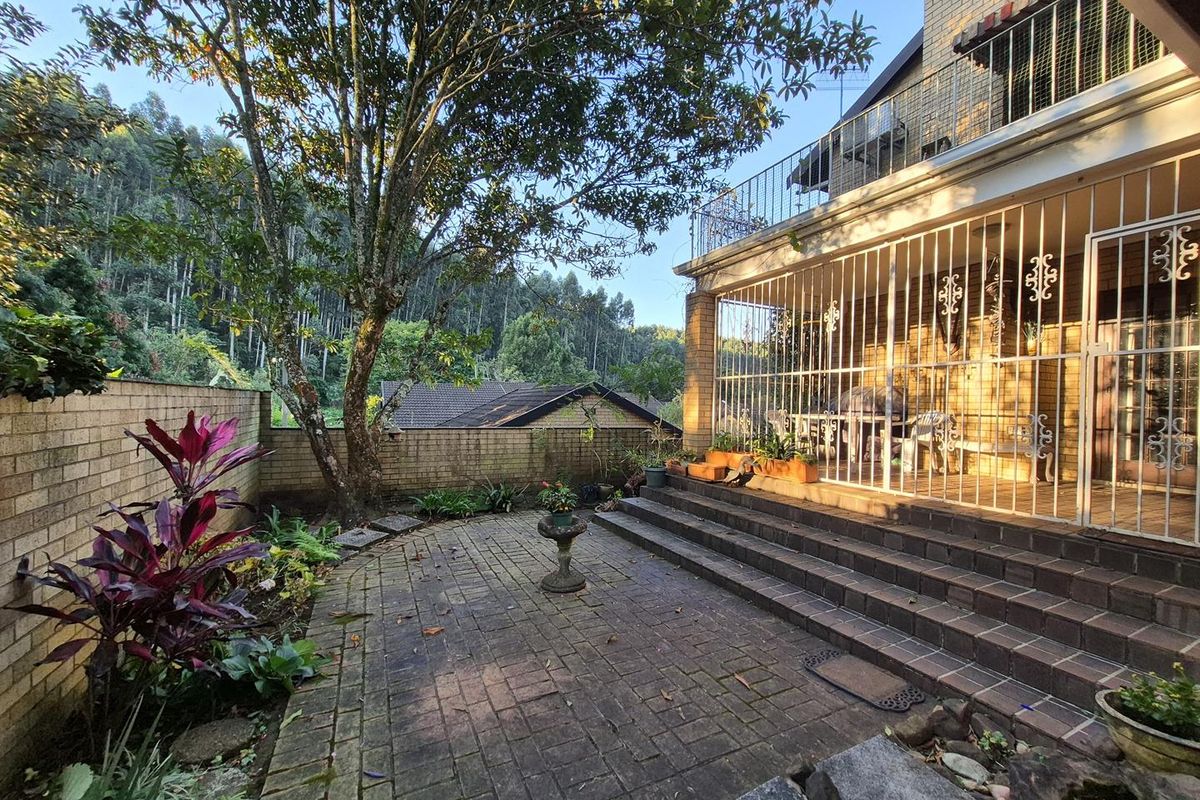 Rear exterior view of the townhouse featuring a brick-paved patio, tiered stairs, and a balcony with security bars overlooking a garden area.
