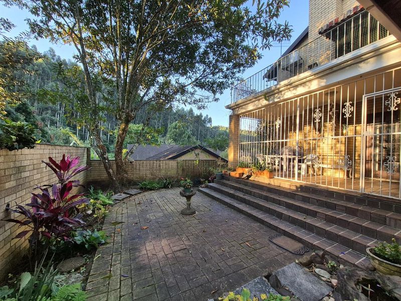 Rear exterior view of the townhouse featuring a brick-paved patio, tiered stairs, and a balcony with security bars overlooking a garden area.