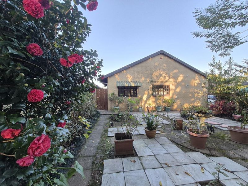 A rear view of the townhouse featuring a brick facade, paved patio area, and established garden surroundings.