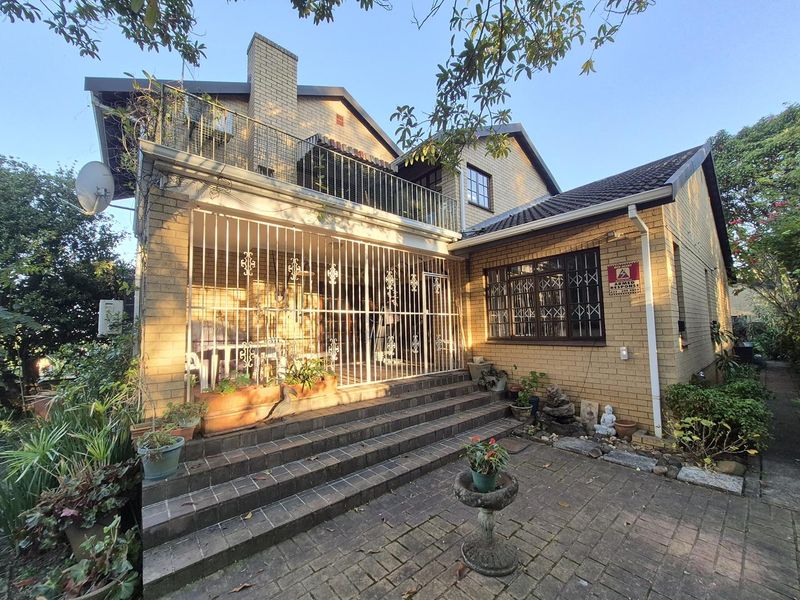 Rear view of a brick townhouse featuring a paved patio area, an upper-level balcony with metal railings, and security bars on ground-floor windows.