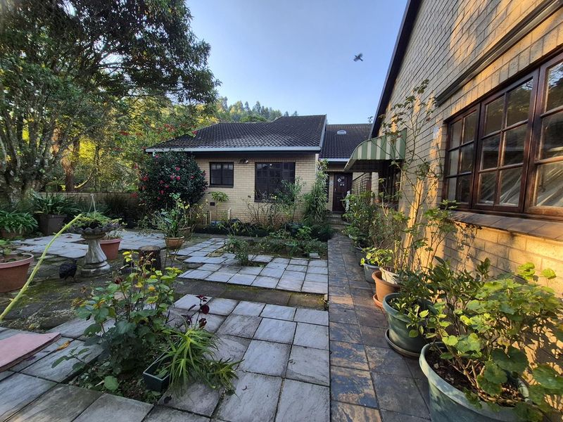 A rear exterior view of the townhouse featuring a paved courtyard area, brick facade, and established garden surroundings.