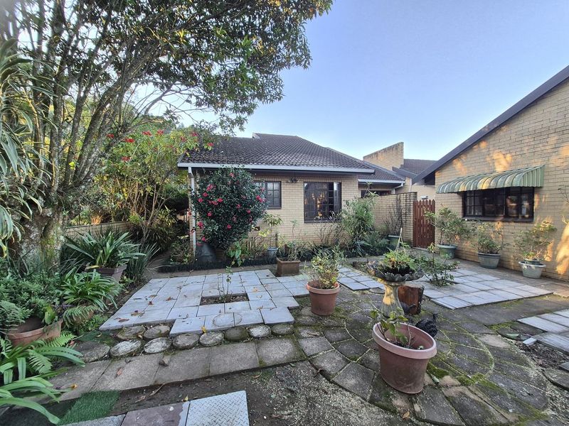 A rear exterior view of a brick townhouse featuring a paved patio area, established garden, and security-fitted windows.