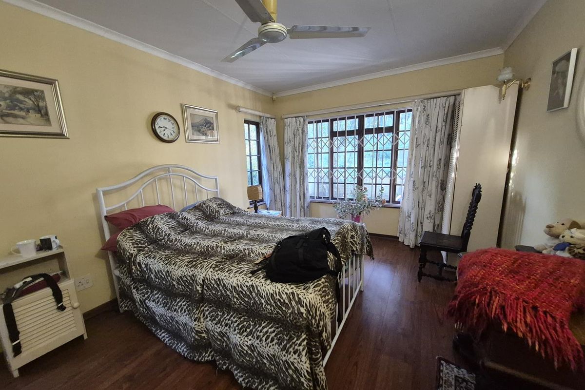A bedroom featuring laminate flooring, a ceiling fan, and large windows with security bars, offering a functional space with potential for modern updates.