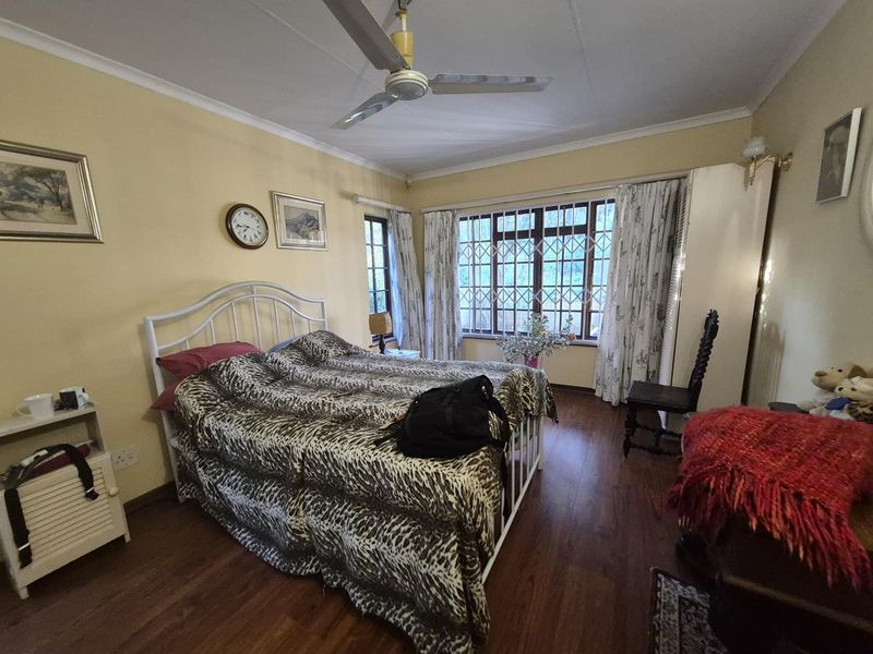 A bedroom featuring laminate flooring, a ceiling fan, and large windows with security bars, offering a functional space with potential for modern updates.