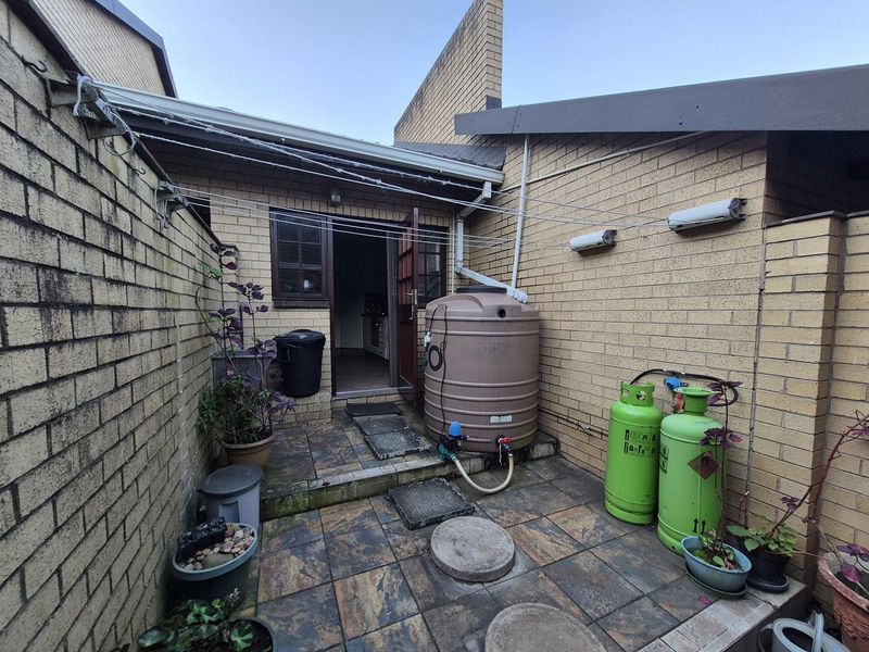 A functional rear courtyard area featuring brick walls, tiled flooring, a water storage tank, and external utility connections.
