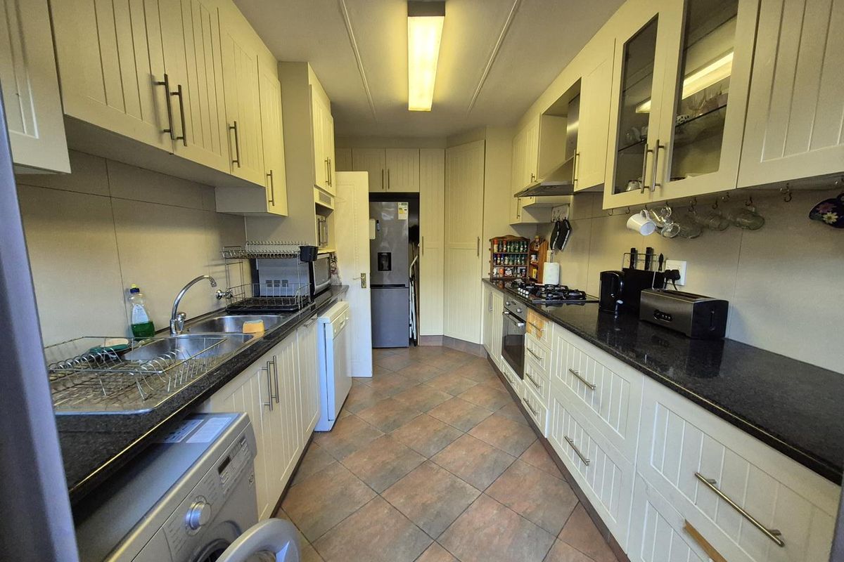 A functional galley-style kitchen featuring cream cabinetry, dark granite countertops, tiled flooring, and integrated appliances including an oven and gas hob.