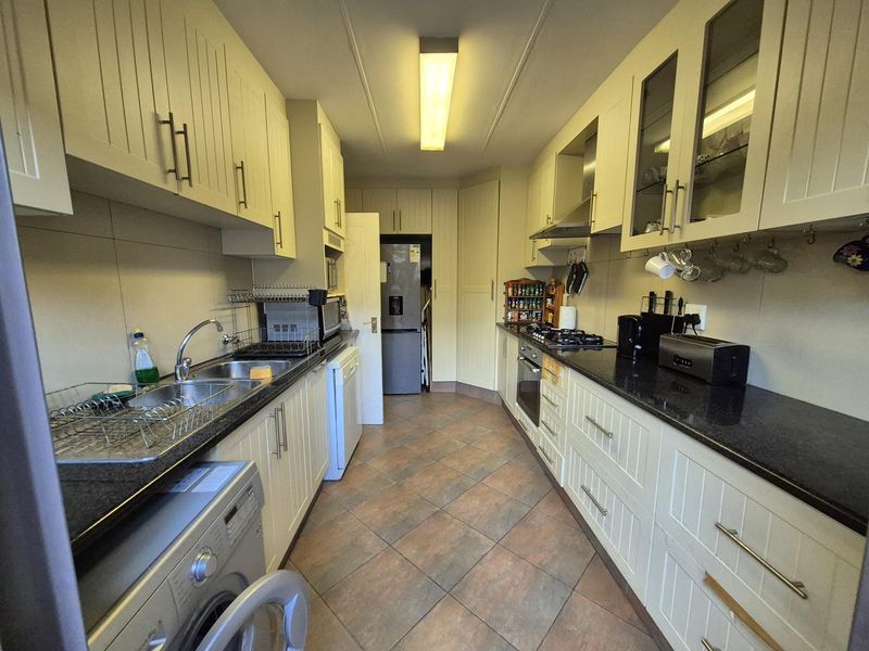 A functional galley-style kitchen featuring cream cabinetry, dark granite countertops, tiled flooring, and integrated appliances including an oven and gas hob.
