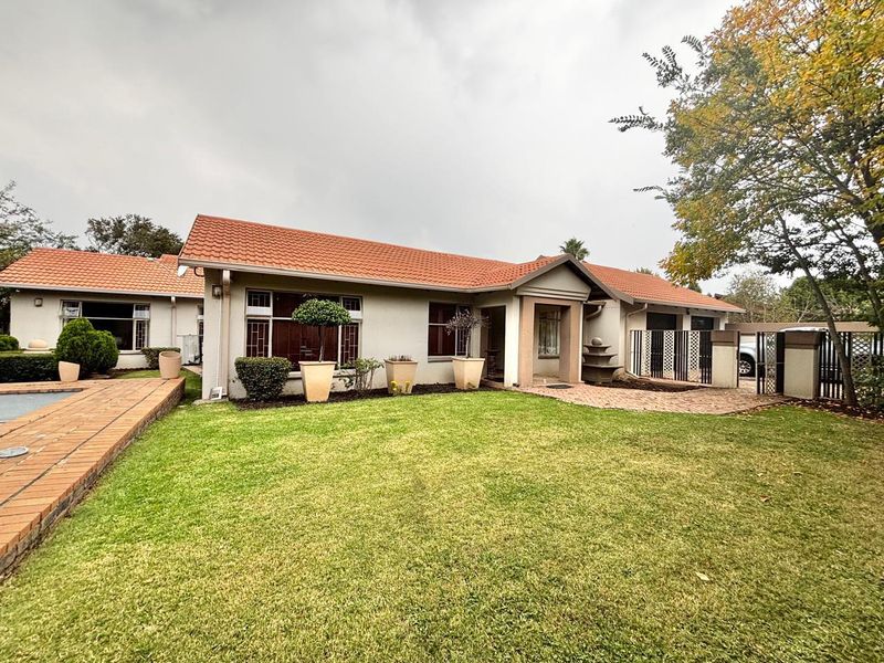 Rear view of the house featuring a well-maintained lawn, brick paved patio area, swimming pool, and a covered entrance porch under a terracotta tiled roof.