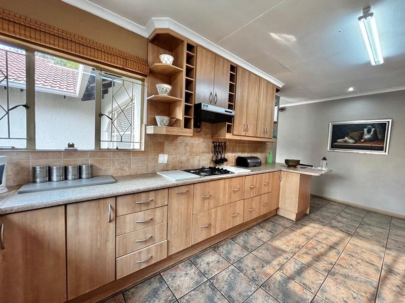 A functional kitchen featuring wood-look laminate cabinetry, tiled backsplash, gas hob with extractor, and durable ceramic floor tiles.