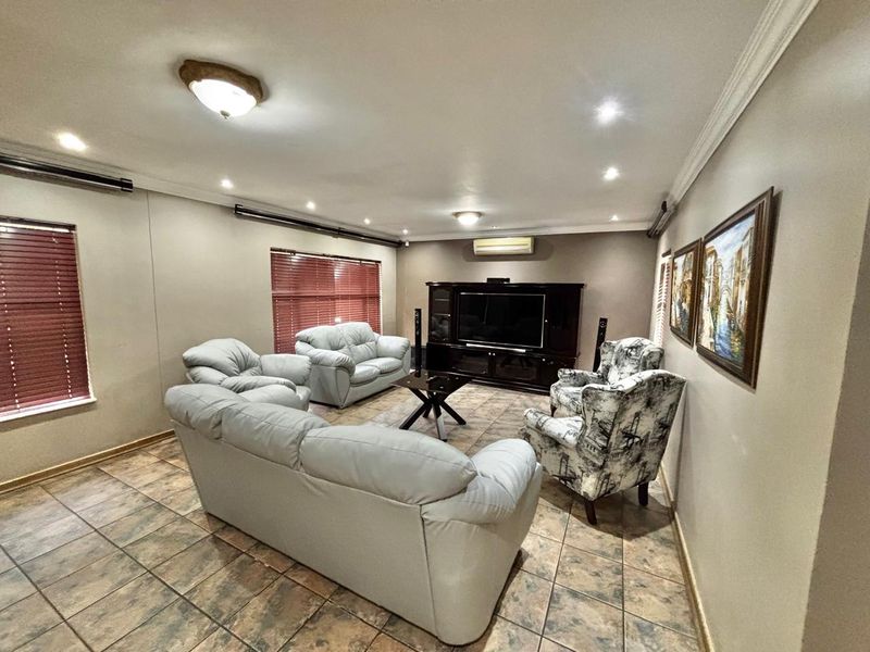 A spacious living room featuring tiled flooring, crown molding, recessed lighting, and a wall-mounted split-system air conditioner.