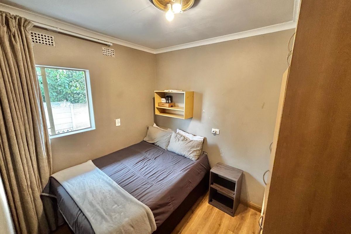 A compact bedroom featuring laminate flooring, neutral wall tones, and a wall-mounted storage shelf.
