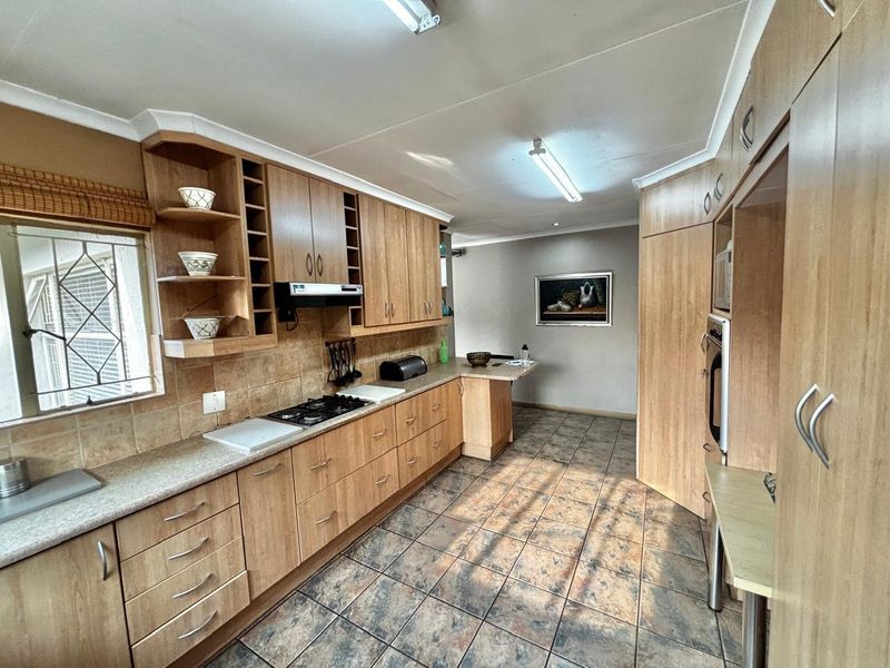 A functional kitchen featuring wood-look laminate cabinetry, a gas hob with extractor, built-in oven, and durable tiled flooring throughout.