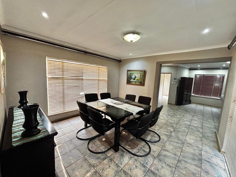 A functional dining room featuring tiled flooring, recessed lighting, and venetian blinds, with an open-plan flow into the adjacent living area.