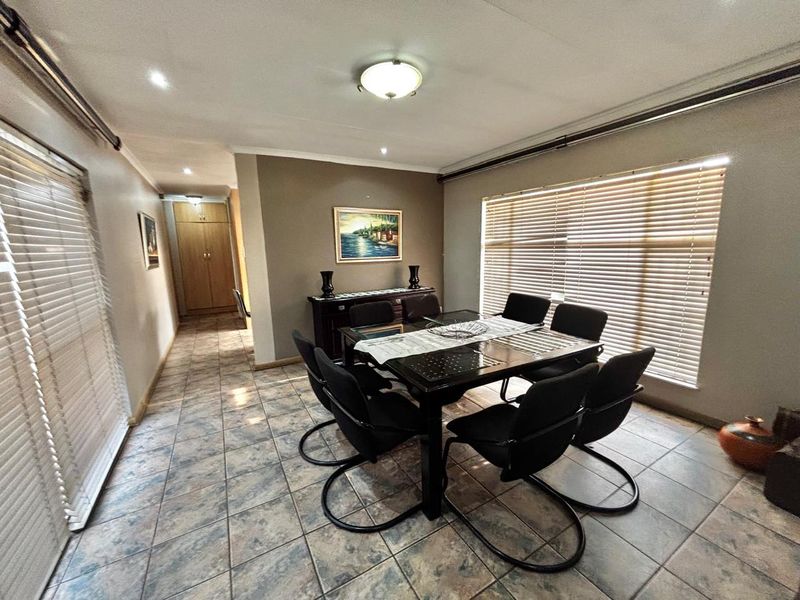 A dining room featuring tiled flooring, venetian blinds, and recessed lighting, with a hallway leading to built-in storage cupboards.