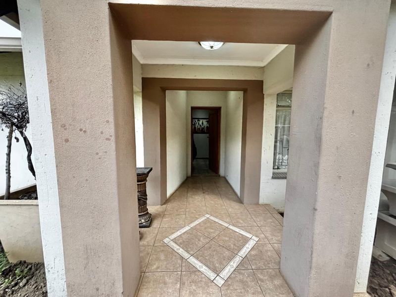 A covered entrance porch featuring tiled flooring with a decorative inlay and plastered structural pillars leading to the main front door.