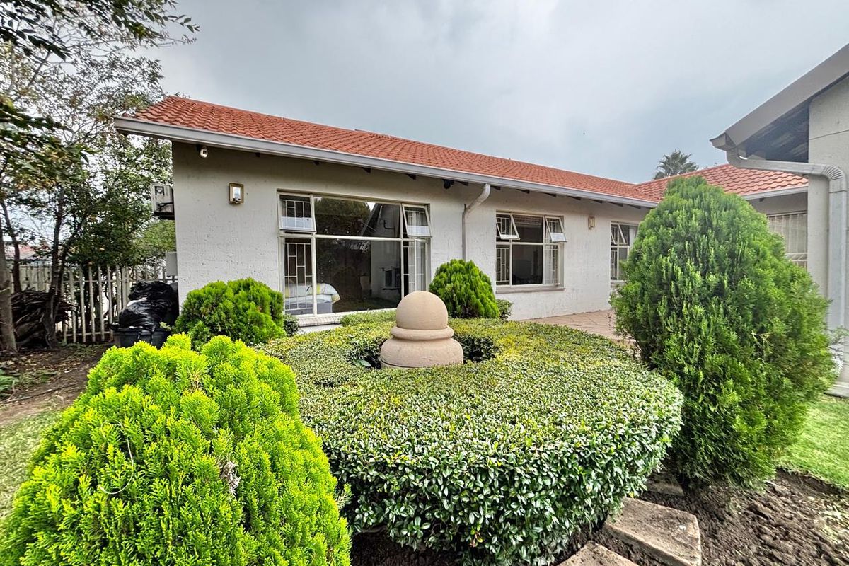 Rear view of the property featuring a terracotta tiled roof, stucco facade, and a landscaped garden with a central stone feature.