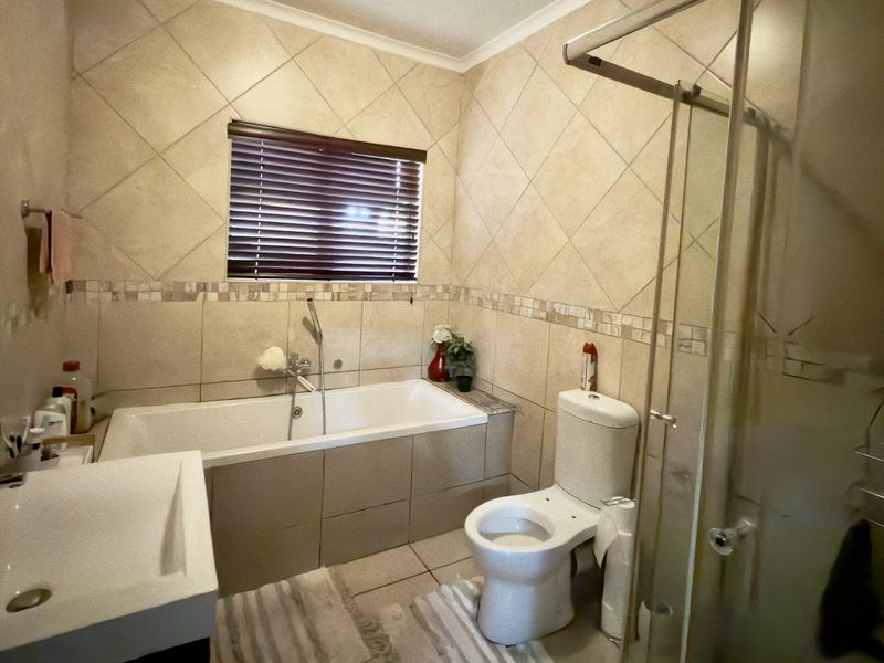 A functional bathroom featuring a built-in bathtub, separate shower enclosure, toilet, and vanity basin with neutral wall and floor tiling.