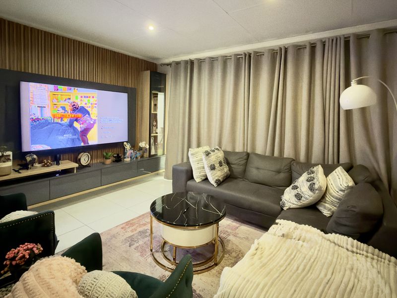 A well-maintained living room featuring a modern slatted wood accent wall, built-in media cabinetry, and neutral tiled flooring.