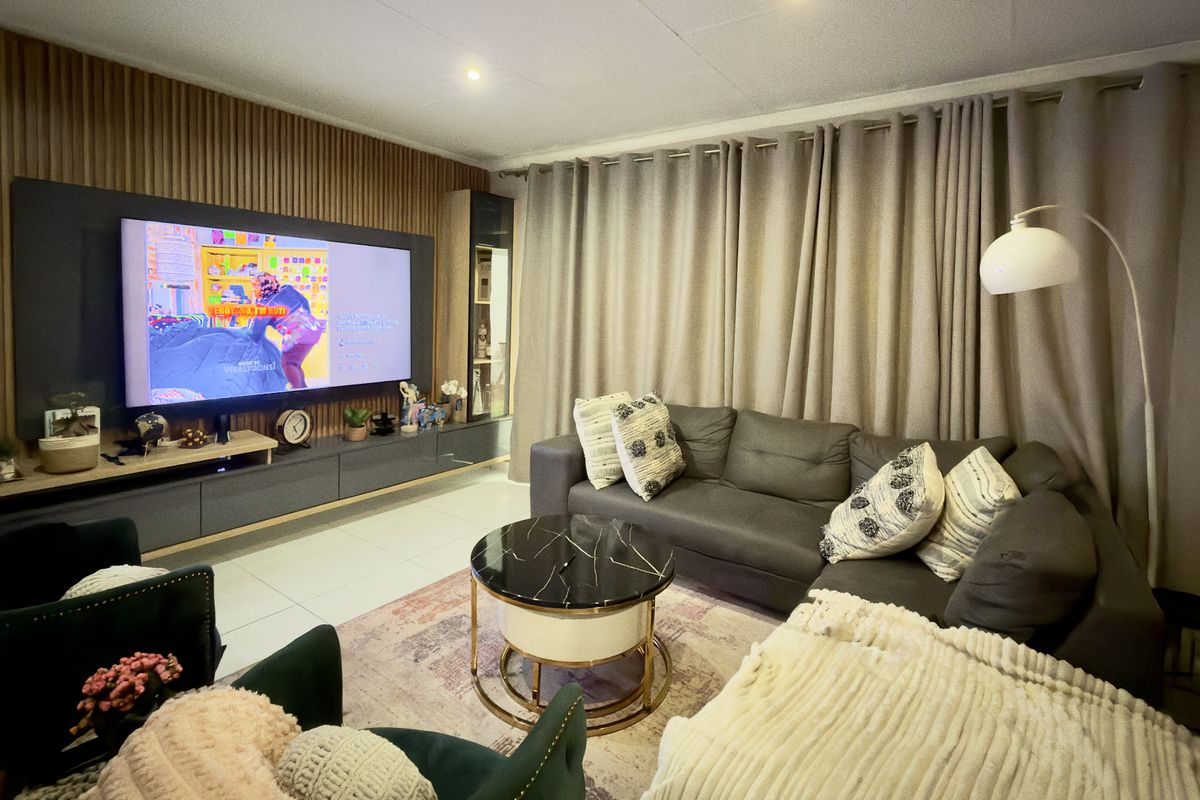 A well-maintained living room featuring a modern slatted wood accent wall, built-in media cabinetry, and neutral tiled flooring.