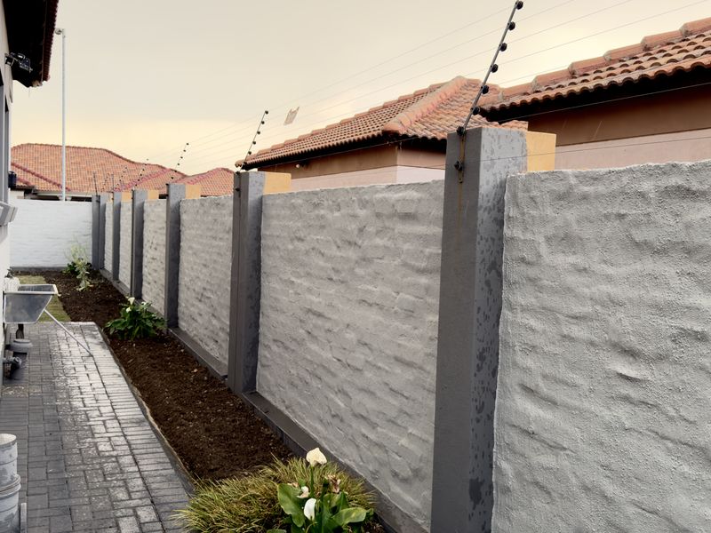 A side exterior view featuring a textured boundary wall with integrated electric fencing and a neat paved walkway.