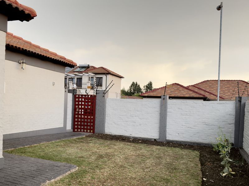 A view of the rear garden area featuring a paved walkway, perimeter wall with electric fencing, and a secure metal gate.