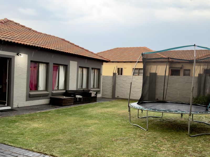 Rear view of the property featuring a tiled roof, paved patio area, and a private garden enclosed by a perimeter wall with electric fencing.