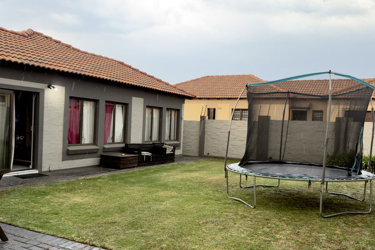 Rear view of the property featuring a tiled roof, paved patio area, and a private garden enclosed by a perimeter wall with electric fencing.