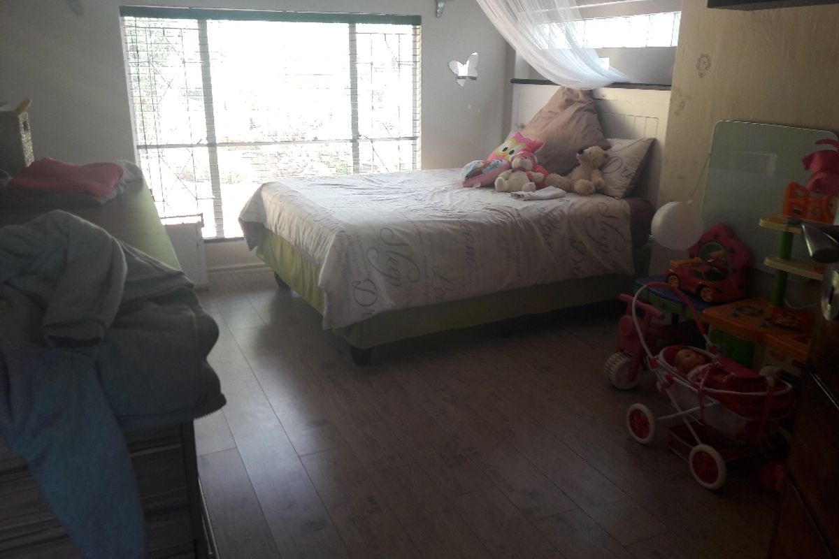 A bedroom featuring laminate flooring and a large window with security bars, providing natural light.