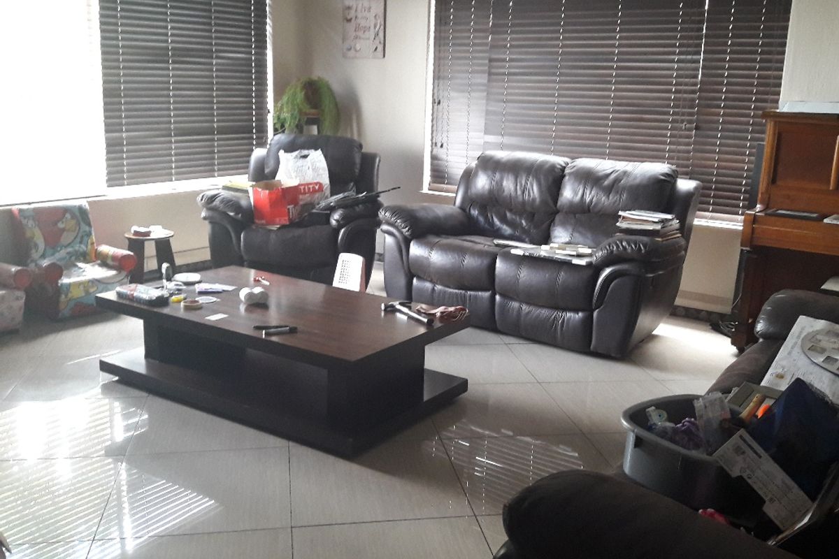 A spacious living room featuring large windows with venetian blinds and neutral tiled flooring throughout.