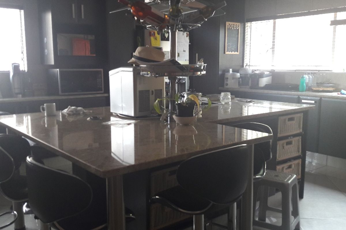 A modern kitchen featuring a large granite-topped island, dark cabinetry, and built-in appliances, providing a functional and stylish culinary space.